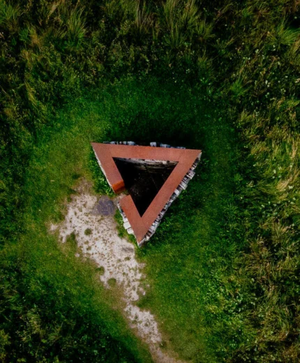 Aerial view of a triangular stone shelter surrounded by lush greenery in a serene setting.