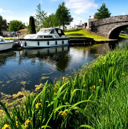 Families enjoying a sunny day by canal boats and stone bridge.