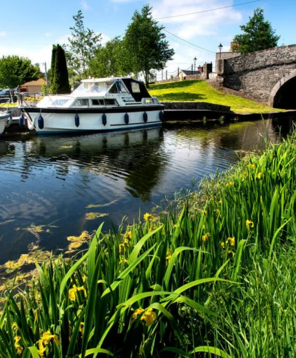 Families enjoying a sunny day by canal boats and stone bridge.