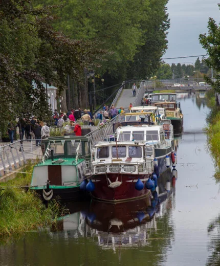 Families exploring canal with docked boats and lush greenery.