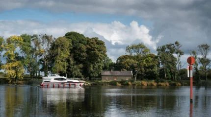 A couple enjoys a peaceful boat ride on a serene lake surrounded by lush greenery and a cosy cottage.