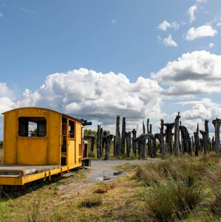 Vintage yellow train car in scenic rural landscape with blue sky and clouds.