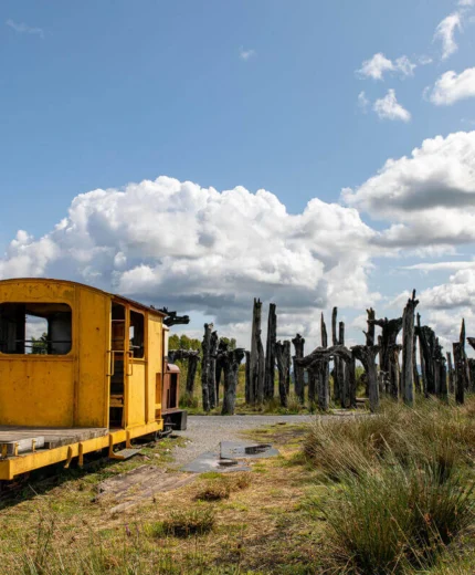 Vintage yellow train car in scenic rural landscape with blue sky and clouds.