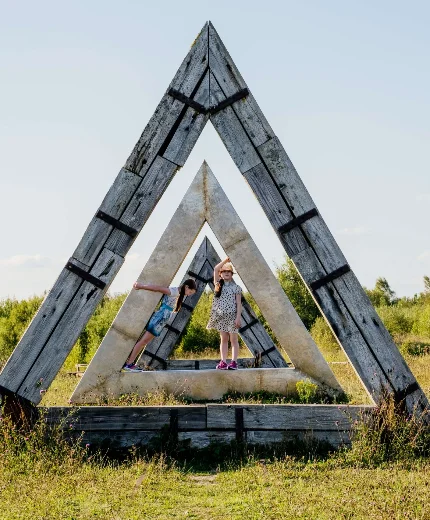 Children playing in large wooden triangle structure in a sunny meadow.