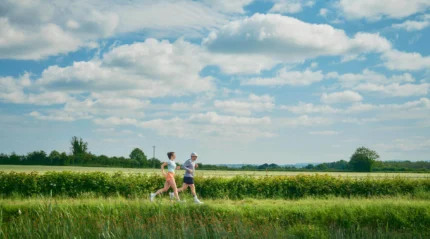 A couple jogging through a lush countryside on a sunny day.