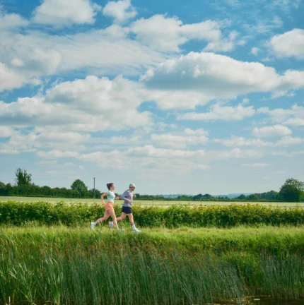 A couple jogging through a lush countryside on a sunny day.