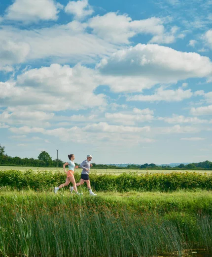 A couple jogging through a lush countryside on a sunny day.