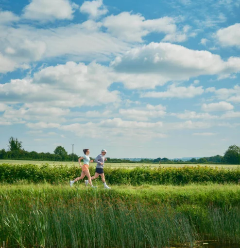 A couple jogging through a lush countryside on a sunny day.