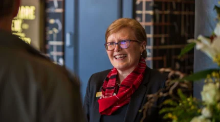 Friendly hotel receptionist warmly greets guests with a smile in a welcoming lobby.