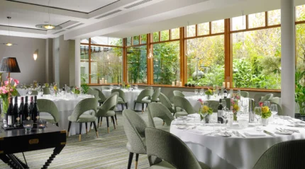 Elegant dining room in a resort with round tables set for guests, large windows revealing lush greenery.