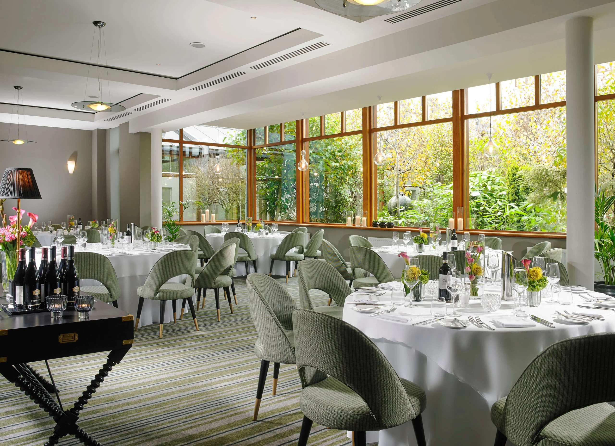Elegant dining room in a resort with round tables set for guests, large windows revealing lush greenery.