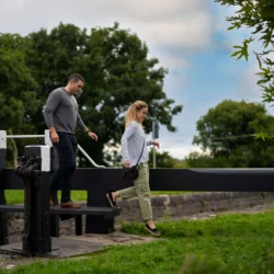 Couple enjoying a walk near a lock gate in a lush countryside setting.