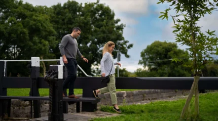 Couple enjoying a walk near a lock gate in a lush countryside setting.