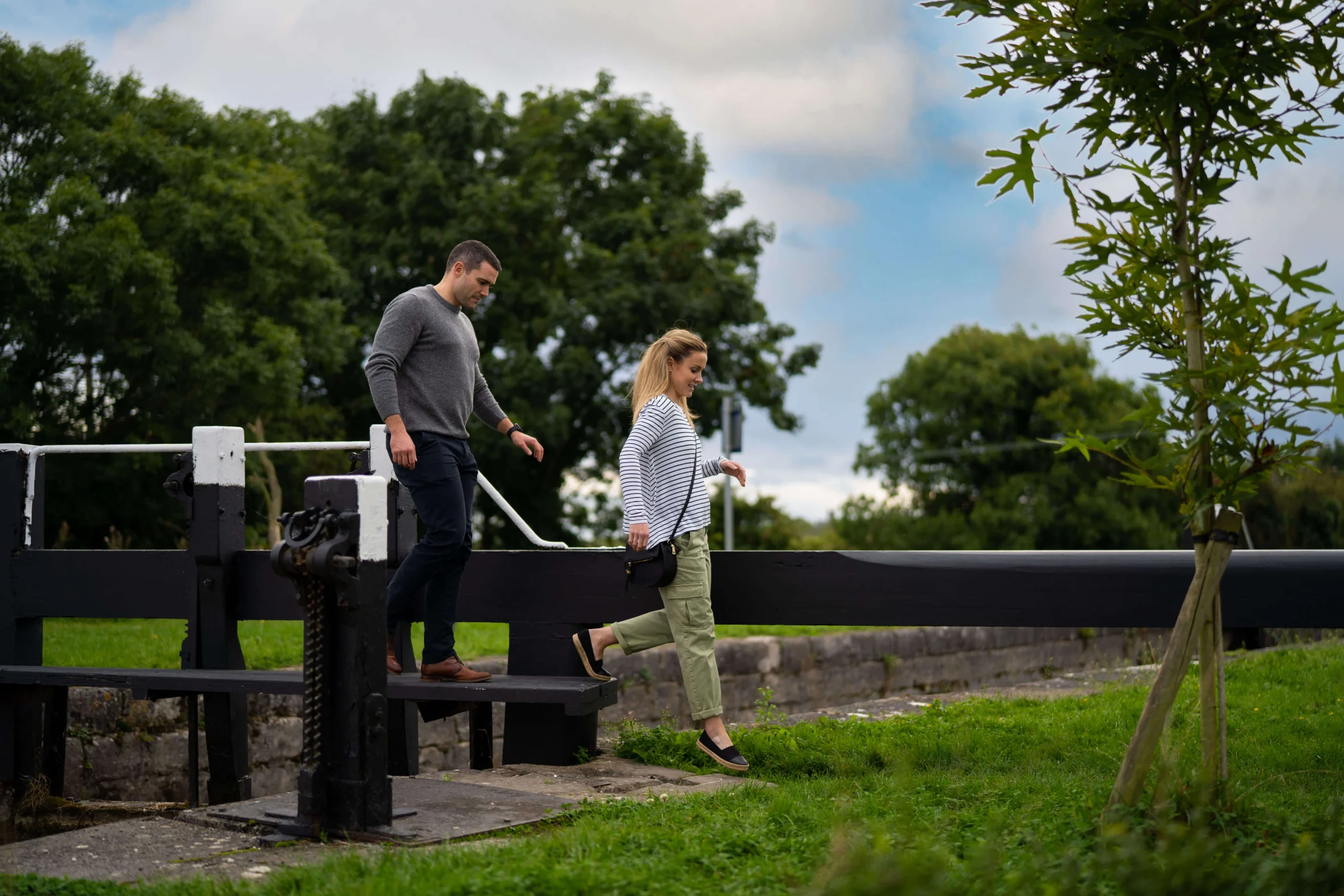 Couple enjoying a walk near a lock gate in a lush countryside setting.