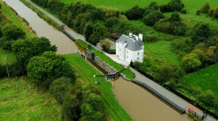Aerial view of a riverside hotel with lush greenery surrounding a scenic canal.