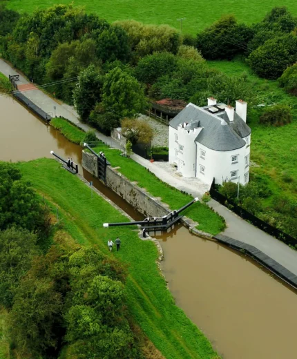 Aerial view of a riverside hotel with lush greenery surrounding a scenic canal.