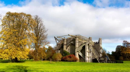 Historic fortress ruins in lush autumn parkland under a blue sky with fluffy clouds.