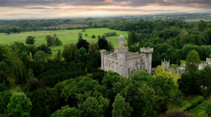 A historic castle nestled in lush green landscapes under a pastel sunset sky.