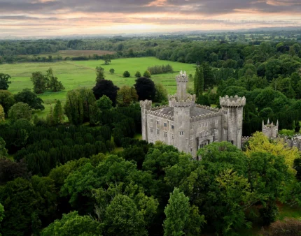 A historic castle nestled in lush green landscapes under a pastel sunset sky.