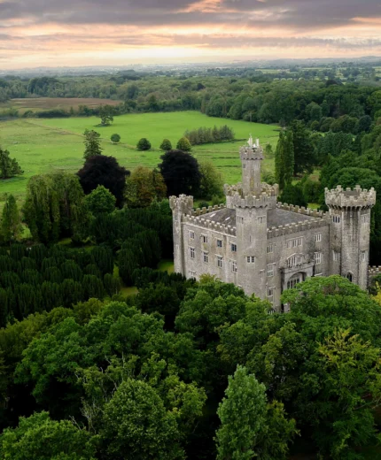 A historic castle nestled in lush green landscapes under a pastel sunset sky.