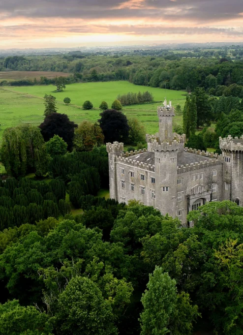 A historic castle nestled in lush green landscapes under a pastel sunset sky.