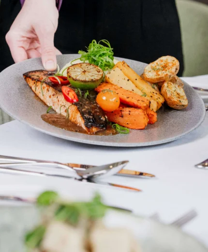 Server presents delicious plated meal in elegant restaurant setting.