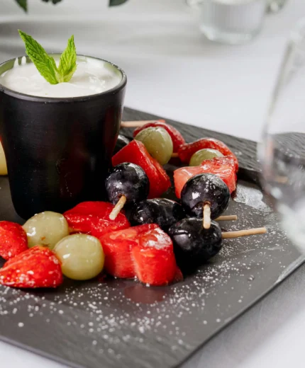 Fresh fruit skewers and dessert on a stylish slate plate, offering a fine dining experience.