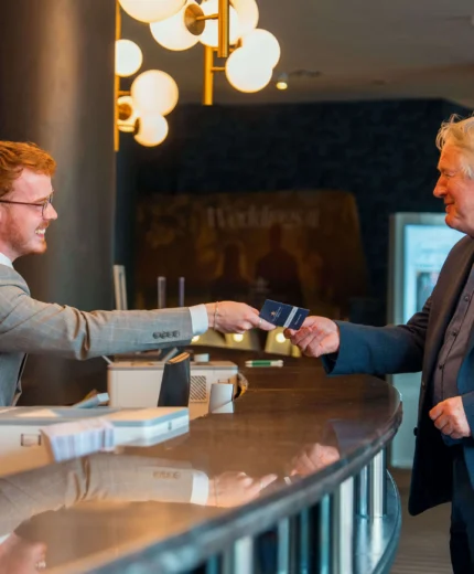 Hotel receptionist warmly greets guest at elegant front desk.