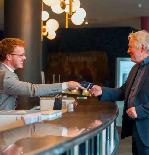Hotel receptionist warmly greets guest at elegant front desk.