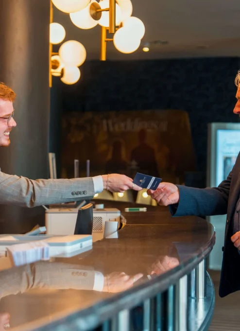 Hotel receptionist warmly greets guest at elegant front desk.