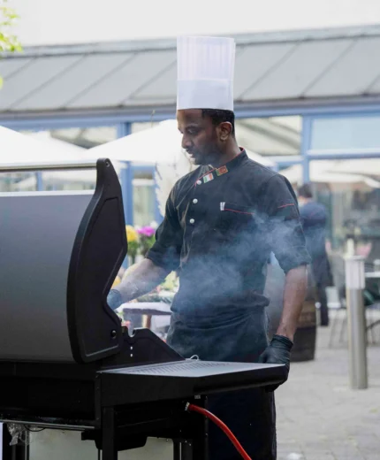 A chef in uniform cooking at an outdoor grill at a resort.