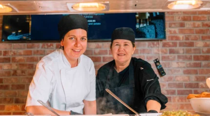 Two friendly chefs smiling in a warm hotel kitchen, preparing dishes together.
