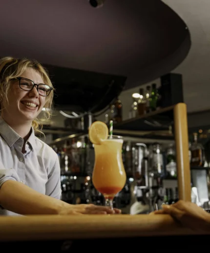 Smiling bartender serves a cocktail to a guest in a cosy hotel bar.