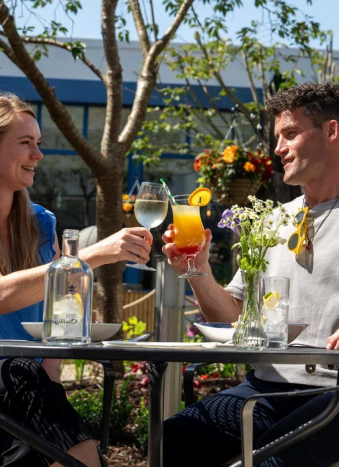 A couple toasting drinks in a sunny hotel garden.