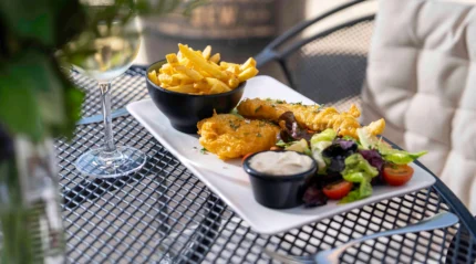 Alfresco dining with fish and chips, salad, and wine at a cosy restaurant.