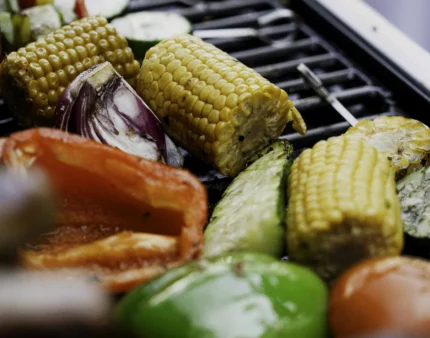 Grilled vegetables including corn, peppers, and zucchini on a barbecue grill.
