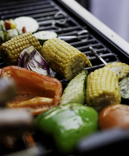 Grilled vegetables including corn, peppers, and zucchini on a barbecue grill.