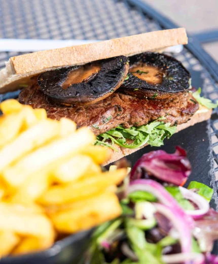 A gourmet sandwich with mushrooms, chips, salad, and a glass of water on an outdoor table.