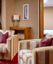Cosy hotel suite with armchairs, inviting decor, and a glimpse of a plush bed.