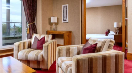Cosy hotel suite with armchairs, inviting decor, and a glimpse of a plush bed.