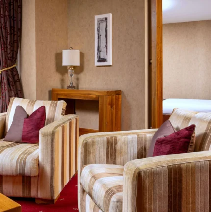 Cosy hotel suite with armchairs, inviting decor, and a glimpse of a plush bed.