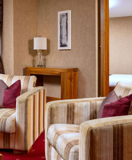 Cosy hotel suite with armchairs, inviting decor, and a glimpse of a plush bed.