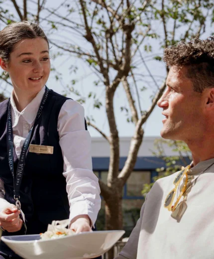 Attentive staff serving a relaxed guest at an outdoor dining area on a sunny day.