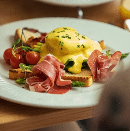 Elegant breakfast with eggs Benedict, tomatoes, and cured meat in a cosy dining setting.