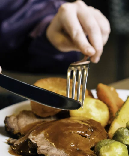 A person enjoys a hearty roast dinner with vegetables at a cosy restaurant.