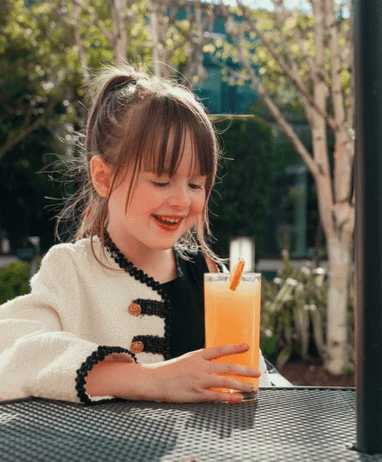 Cheerful child enjoying a fresh juice outdoors at a sunny resort café.