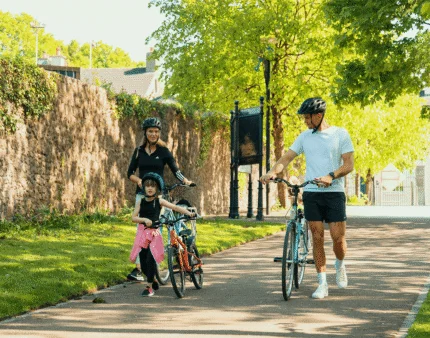 Family cycling along a sunny path with lush greenery.