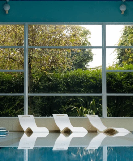 Sun loungers by indoor pool in serene hotel spa, large window with garden view.