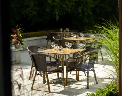 Sunny outdoor dining area with empty tables and lush greenery at a resort.