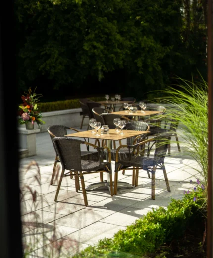 Sunny outdoor dining area with empty tables and lush greenery at a resort.